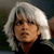 Pixelated close-up of a person with short white hair wearing a dark top against a blurred background.