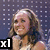 A woman in a white off-shoulder dress holds a microphone, smiling against a dark dotted background with 'x1' text overlays.