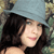 A static pixelated image shows a person with long dark hair, light skin, and a slight smile, set against a blurred background with muted tones.
