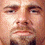 Pixelated close-up of a human face with light skin tone, visible eyes, nose, mouth, and partial neck area in warm brown and beige tones.