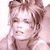 Pixelated close-up of a person with light brown hair styled in a voluminous, slightly messy updo, wearing a light-colored garment with visible folds.