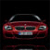 Red car front view with headlights, grille, and license plate on dark background.