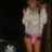 A person in a white sweater and pink shorts stands against a dark background with two circular lights visible.