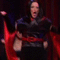 A woman in black clothing with a red sash performs dynamic poses against a red curtain backdrop, her red cape flowing in motion.