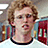 A pixelated image of a person with curly light brown hair wearing a white shirt with a black collar, set against a light blue background with red text.