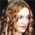 A pixelated close-up of a person with long curly brown hair, light skin, and red lips against a dark background.