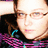Pixelated close-up of a person with light skin tone wearing glasses, dark hair, and a dark top with pink and blue accents.