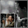 A person in a dark jacket holds a microphone near their mouth, with background elements shifting across frames.