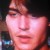 Pixelated close-up of a person's face with reddish skin tones, dark hair, and a neutral expression against a dark background.