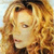 Pixelated close-up of a person with light brown curly hair, wearing dark clothing against a light background.