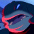 A pixelated circular icon with a dark blue background, featuring a glowing light blue oval shape and swirling pinkish-red patterns against a gradient backdrop.