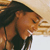 A pixelated close-up of a person with dark hair and brown skin, mouth open in a shout or yell, against a light brown background.