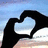 Black silhouette hands forming a heart shape against a gradient sky background with light blue and white tones.