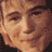 Pixelated close-up of a person's face with light brown hair and closed eyes, rendered in warm tones on a dark background.