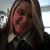 A person with long light brown hair wearing a dark jacket and white collar, smiling in a of four with varying brightness and cropping