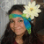 A pixelated portrait of a person with long dark hair wearing a green and blue headband, holding a large white flower near their face.