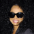 Pixelated image of a person with light skin tone wearing dark sunglasses, smiling with visible teeth, against a dark background.