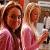 Two figures in pink garments stand side-by-side against a blurred background with warm tones and indistinct shapes.