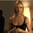 Pixelated static image of a woman with long brown hair wearing a black strapless top, seated in front of a bright light source on the right side.