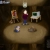 A pixelated scene shows a figure in maroon top and blue pants standing behind an oval table with two objects, against dark wooden paneling.