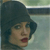 Pixelated close-up of a person wearing a dark blue hat with a wide brim, mouth open in a surprised expression, against a blurred background with green and gray tones.