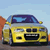 Pixelated yellow car with dark blue roof, black grille, and visible headlights against light blue sky background.