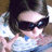 A person with brown hair wearing dark sunglasses and a light blue patterned shirt makes a peace sign gesture in three