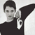 Pixelated grayscale image of a person with short dark hair wearing a dark shirt, holding a large black object with a white section featuring a dark symbol.