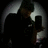 Pixelated grayscale image of a figure with dark hair and light clothing against a black background, showing partial facial features and a curved light shape on the left.