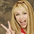 A pixelated image of a person with long blonde hair making a peace sign gesture, wearing red clothing against a blurred background.