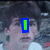 A pixelated image of a person with dark hair and light skin, wearing a white shirt against a blurred background.