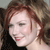 Pixelated close-up of a person with reddish-brown hair, closed eyes, and a slight smile, wearing a dark top against a blurred background.