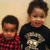 Two children stand side-by-side against a light beige background; the child on the right wears a dark shirt with a light-colored graphic design.