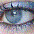 A pixelated close-up of a human eye with blue and purple hues, featuring visible eyelashes and a reflective highlight on the iris.