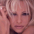 Pixelated close-up of a person with short light-colored hair, dark eyes, and a neutral expression, wearing a dark top against a blurred background.