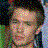 Pixelated static image of a person's face with blurred features, surrounded by multicolored pixel blocks in green, blue, and black tones.