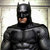 Pixelated image of a figure in a black cowl with pointed ears, dark mask covering eyes, and armored chest plate, standing against a light background.