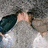 Pixelated image of a person with light skin and brown hair lying down, wearing a dark green top and light gray pants against a gray background.