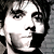 Black-and-white pixelated close-up of a person's face with dark hair, visible eyes, nose, mouth, and jawline against a gray background.