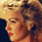 Pixelated close-up of a person's face with curly hair, red lips, and warm-toned skin against dark background.