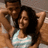 Two people embrace; one wears a light blue sleeveless top, the other has dark hair and brown skin tones.