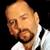 Static pixelated image of a bald man with light skin, brown facial hair, and closed eyes wearing a white shirt against black background.