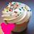 Pixelated static image of a cupcake with white frosting, chocolate chips, and a bright pink bow on the base.