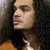 A person with long curly hair wears an orange jacket over a white shirt, shown in three with slight head position changes
