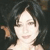 Pixelated close-up of a person with dark hair and light skin, wearing a light-colored top against a dark background.