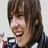 Pixelated close-up of a person with brown hair and light skin smiling broadly, wearing dark clothing against a plain background.