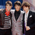 Three individuals in formal attire stand side-by-side with arms around each other against a dark blue background.