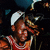 A pixelated figure in a red and white basketball jersey, white headband, and dark shorts smiles while raising an arm to shield eyes from light.