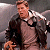 Pixelated image of a person in a dark jacket over a light shirt with a white collar, standing against a gray background.