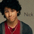 A person with dark curly hair wears a red shirt and gray cardigan, standing against a light brown background with 'Nick' text visible.